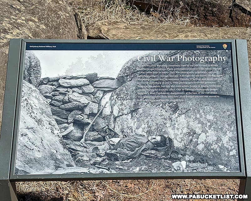 An informational sign about Civil Was photography featuring the image of a deceased Confederate sharpshooter at Devil's Den on the Gettysburg battlefield.