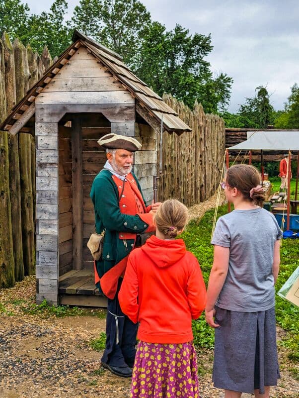 Reenactor in 18th-century attire conversing with two young visitors near a guard shack at Fort Loudoun.