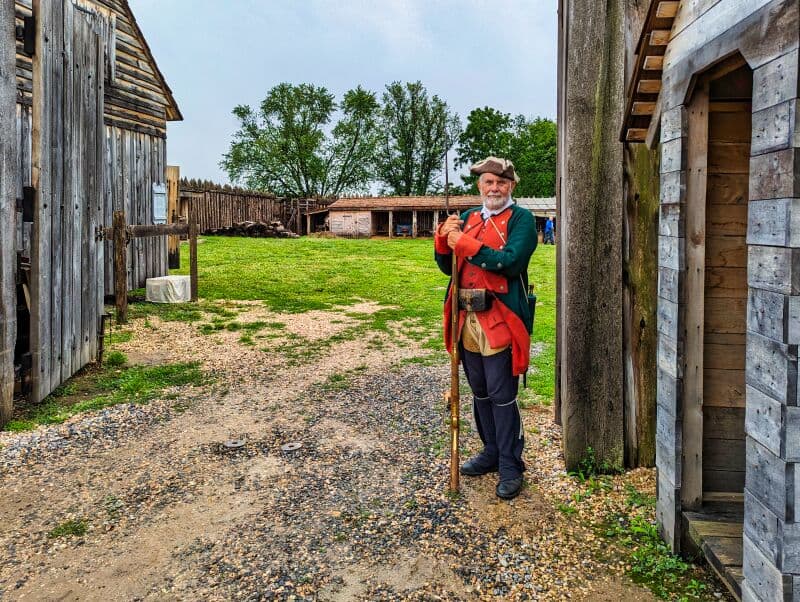 Guard dressed in historical colonial attire, with a green coat and tricorn hat, holding a long musket, standing at the entrance to Fort Loudoun in Franklin County, Pennsylvania