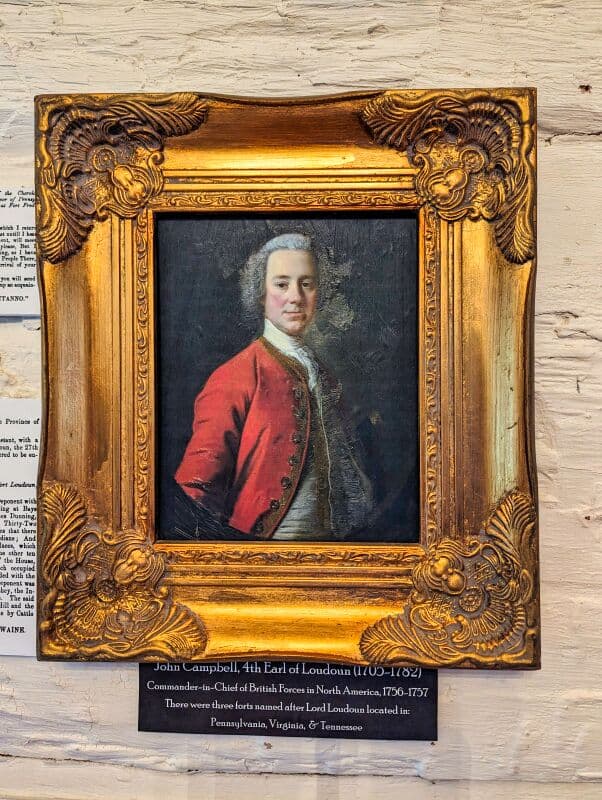 Ornate gold-framed portrait of John Campbell, 4th Earl of Loudoun (1705-1782), displayed against a rustic white wall. The man in the portrait wears a red military coat with decorative buttons and white ruffled shirt. Beneath the painting, a placard reads 'John Campbell, 4th Earl of Loudoun (1705-1782) Commander-in-Chief of British Forces in North America, 1756-1757. There were forts named after Lord Loudoun located in Pennsylvania, Virginia, & Tennessee.' Displayed at Fort Loudoun in Franklin County, Pennsylvania.