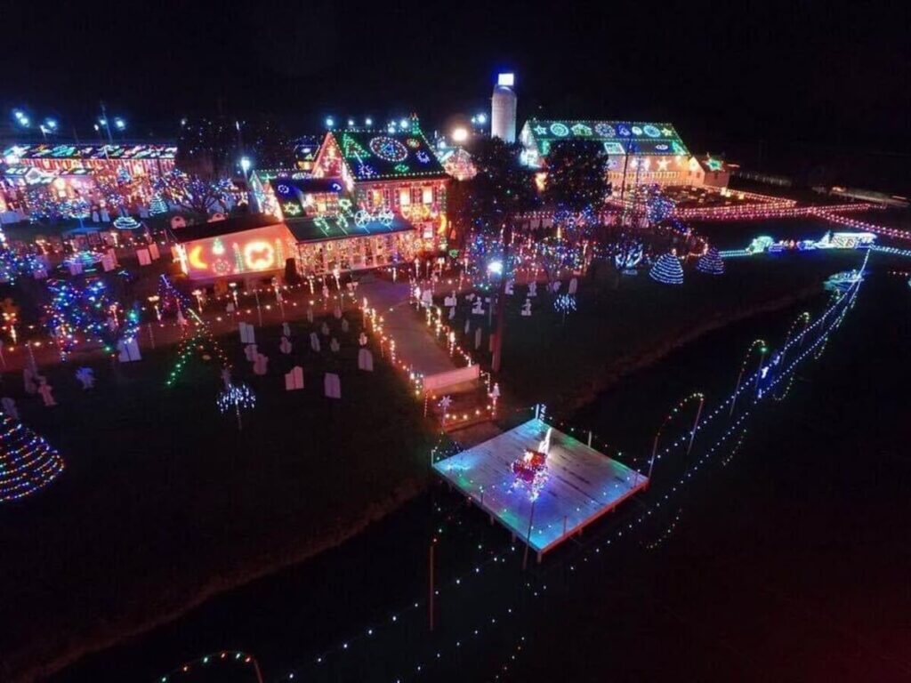 Aerial night view of Koziar's Christmas Village in Berks County, Pennsylvania, showcasing the brightly lit and decorated houses with a multitude of Christmas lights. The festive lights create patterns and designs, illuminating trees, buildings, and walkways throughout the village.