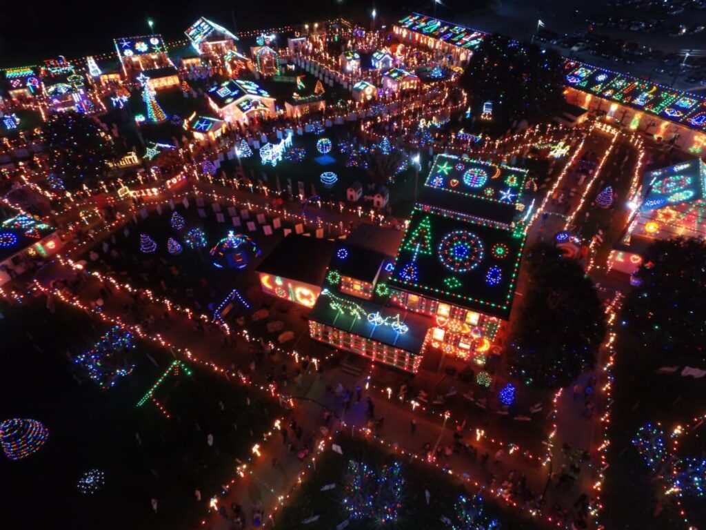 Aerial night view of Koziar's Christmas Village in Berks County, Pennsylvania, illuminated by thousands of twinkling lights. The village is a tapestry of color, with each building and tree wrapped in vibrant lights, and walkways lined with glowing bulbs leading visitors through the festive display.