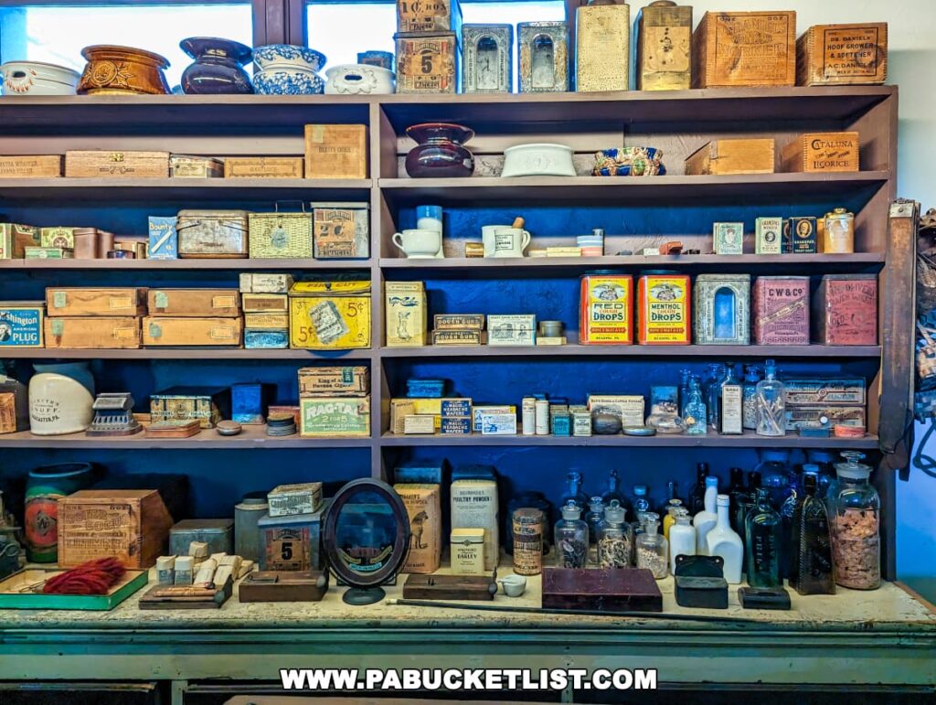 A detailed display of vintage products on wooden shelves at the Landis Valley Museum in Lancaster County, Pennsylvania, resembling an old-time general store. The shelves are filled with an assortment of antique items, including tobacco tins, ceramic bowls, wooden boxes with product labels, glass medicine bottles, and various packaged goods from bygone days.