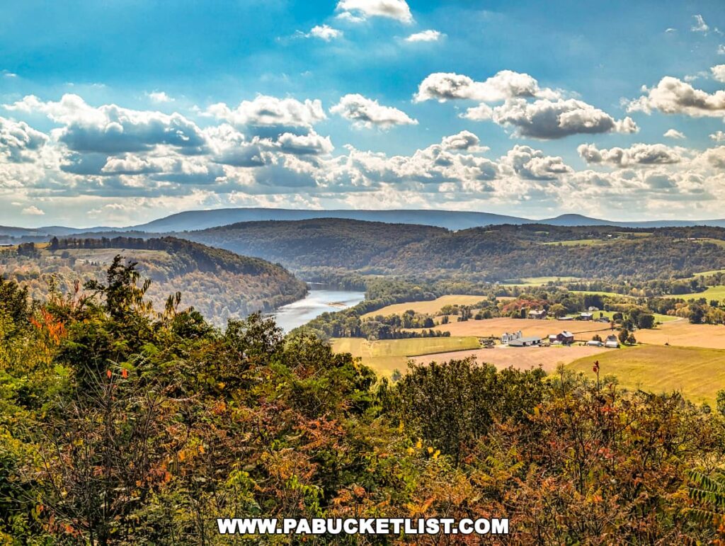 Scenic landscape viewed from the Marie Antoinette Scenic Overlook in Bradford County, Pennsylvania, featuring a serpentine river flanked by lush hills with colorful trees in the foreground and a farm with multiple buildings in the open fields.