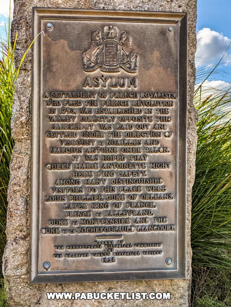 Photograph of a historical plaque titled 'ASYLUM' at the Marie Antoinette Scenic Overlook in Bradford County, Pennsylvania. The bronze plaque commemorates a settlement of French royalists who fled the French Revolution in 1793. Notable figures such as Queen Marie Antoinette are mentioned as potential refugees to the area. The plaque is adorned with an embossed crest and inscribed with the names of distinguished visitors. The Bradford County Historical Society erected the marker in 1936, as noted at the bottom.