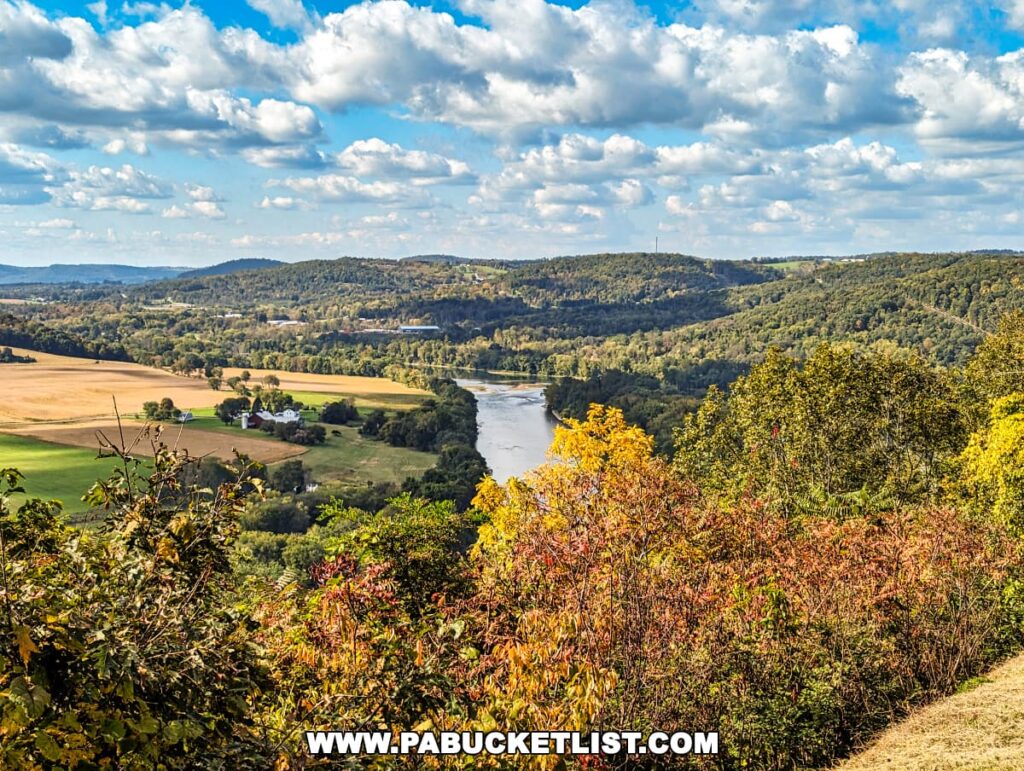 Panoramic view from the Marie Antoinette Scenic Overlook in Bradford County, Pennsylvania, showcasing a sweeping landscape of rolling hills, lush forests, and farmland. A winding river cuts through the valley, with farm buildings nestled among fields.
