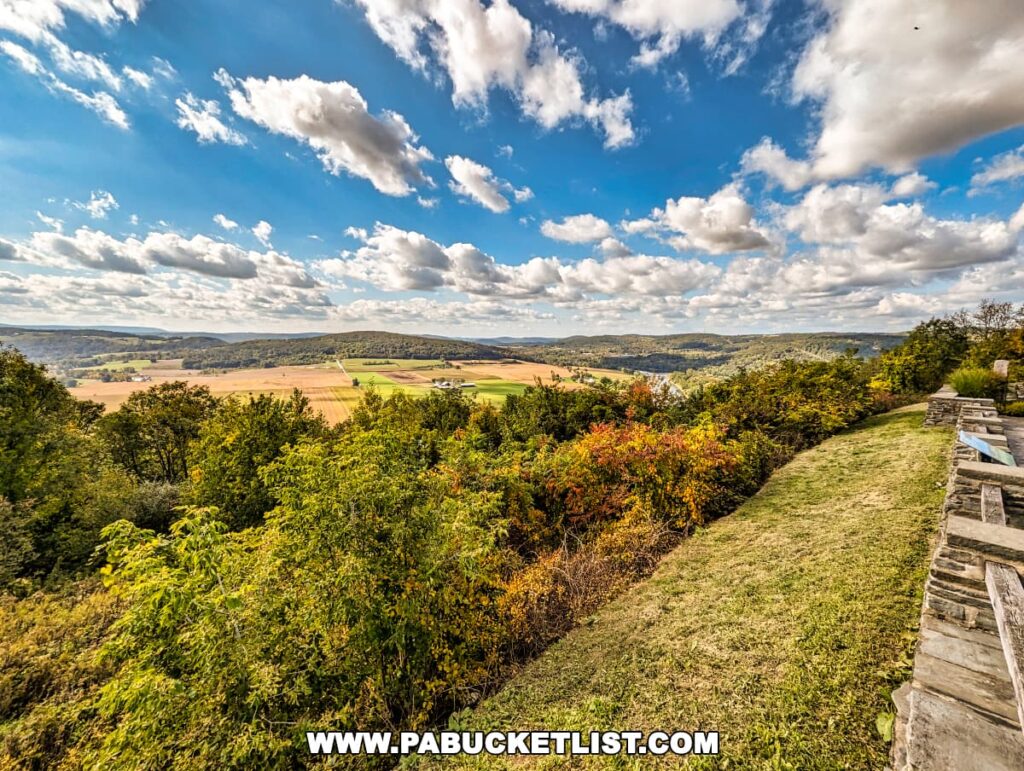 Expansive view from the Marie Antoinette Scenic Overlook in Bradford County, Pennsylvania, showcasing a vast landscape of farmland with patchwork fields. Lush greenery in the foreground transitions to the golden hues of crops. The dynamic sky above is filled with fluffy white clouds scattered across a deep blue.