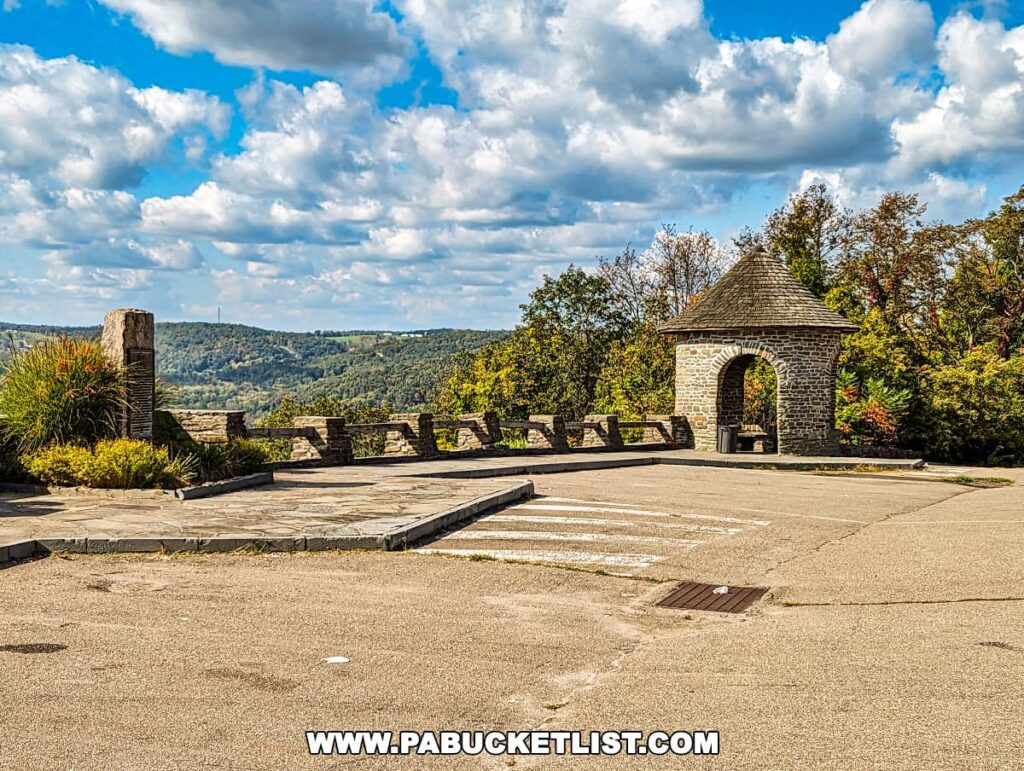 The stone architectural features of the Marie Antoinette Scenic Overlook in Bradford County, Pennsylvania, offering a viewing platform with a stone balustrade and a small stone turret-like structure. The overlook provides a panoramic view of the lush, rolling hills stretching into the distance, framed by a blue sky with abundant white clouds.