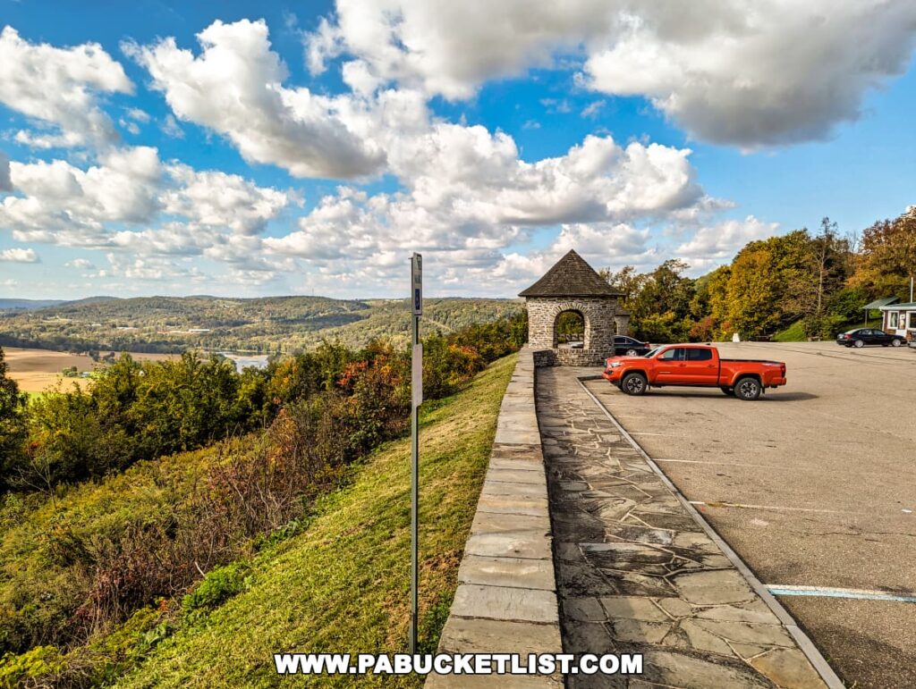 An orange pickup truck parked near a stone gazebo at the Marie Antoinette Scenic Overlook in Bradford County, Pennsylvania. The overlook offers a stunning view of rolling hills, lush greenery, and a winding river in the distance.
