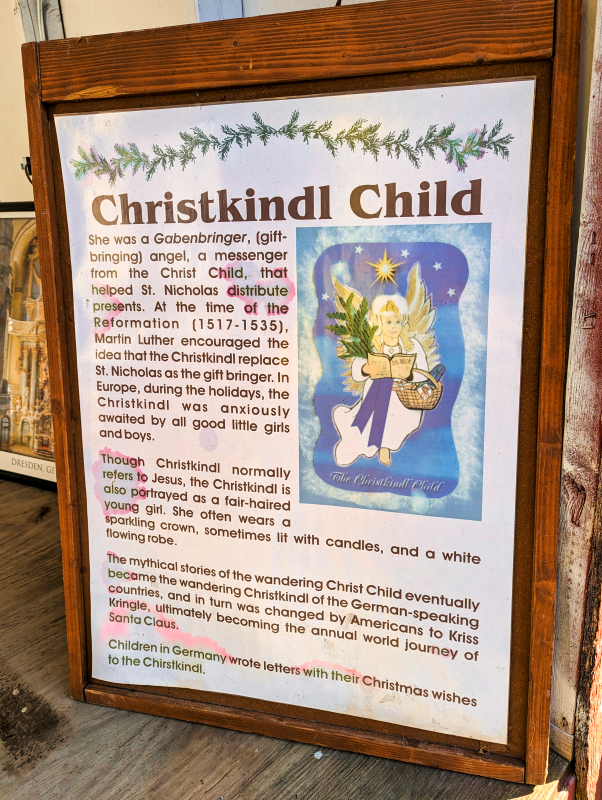 Informational poster about the 'Christkindl Child' with descriptive text and an illustration, detailing its role as a gift-bringer and its evolution in German and American Christmas traditions, displayed at the Mifflinburg Christkindl Market.