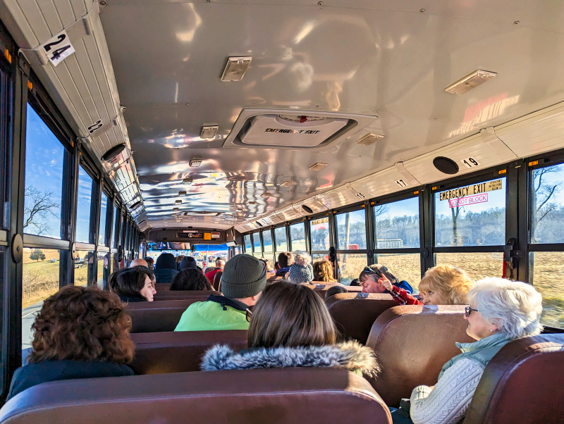 Passengers seated inside a shuttle bus, with sunlight streaming through the windows, while heading to or from the Mifflinburg Christkindl Market in Mifflinburg, Pennsylvania.