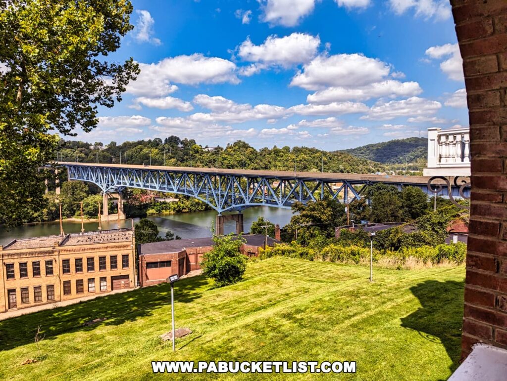 View from Nemacolin Castle of a blue truss bridge over a river, industrial buildings in the foreground, lush trees, and a clear blue sky.
