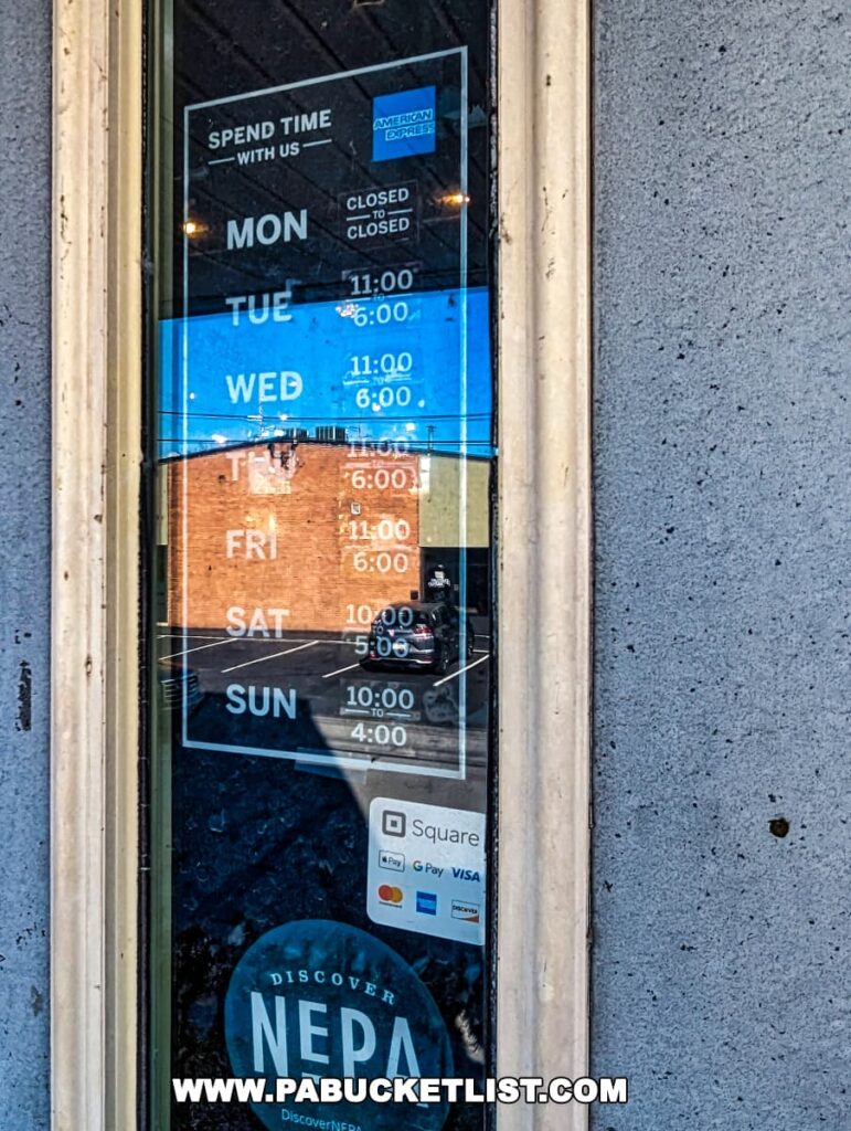 A close-up of the door to On and On in Scranton displaying business hours on a blue and black background. The sign reads 'SPEND TIME WITH US', followed by the days of the week, with opening hours from 11:00 to 6:00 on Tuesday to Friday, 10:00 to 5:00 on Saturday, and 10:00 to 4:00 on Sunday; Monday is closed. Payment logos for Square, Visa, Google Pay, and American Express are visible below, along with a circular logo reading 'DISCOVER NEPA'.