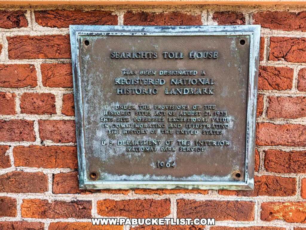 Close-up of a weathered bronze plaque on a red brick wall at Searights Tollhouse, Fayette County, Pennsylvania, declaring it a Registered National Historic Landmark. The text on the plaque, slightly eroded with time, commemorates the designation of the site under the Historic Sites Act of August 21, 1935, and mentions the U.S. Department of the Interior, National Park Service. The date at the bottom of the plaque reads 1964.