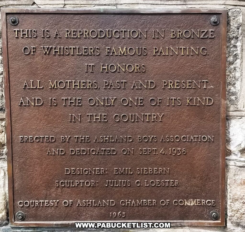 A bronze plaque at the Ashland Mothers Memorial in Ashland, Pennsylvania, with an inscription that reads: 'THIS IS A REPRODUCTION IN BRONZE OF WHISTLERS FAMOUS PAINTING. IT HONORS ALL MOTHERS, PAST AND PRESENT AND IS THE ONLY ONE OF ITS KIND IN THE COUNTRY. ERECTED BY THE ASHLAND BOYS ASSOCIATION AND DEDICATED ON SEPT. 4, 1938. DESIGNER: EMIL SIEBERN SCULPTOR: JULIUS C. LOESTER COURTESY OF ASHLAND CHAMBER OF COMMERCE 1963.' The plaque commemorates the memorial's dedication and its unique status as a tribute to mothers, based on Whistler's famous work.