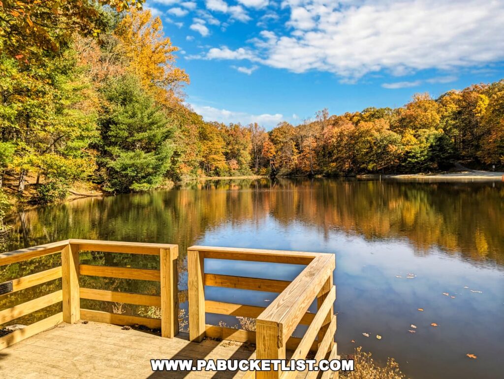 A serene viewpoint at Colonel Denning State Park in Cumberland County, PA, featuring a wooden fishing pier overlooking a calm lake reflecting the vibrant autumn colors of the surrounding foliage, with a backdrop of a clear blue sky and fluffy white clouds.