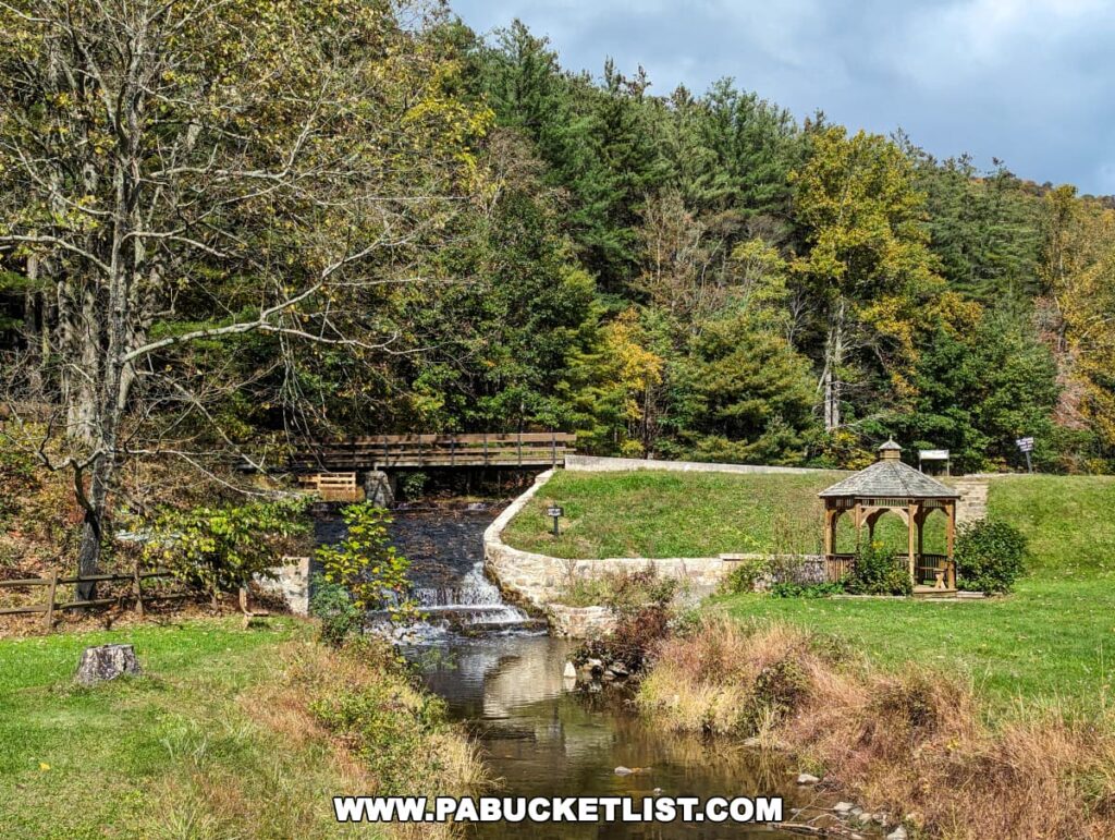 A picturesque view of Colonel Denning State Park in Cumberland County, Pennsylvania. The focal point of the photo is a charming wooden gazebo perched beside a cascading waterfall. The gazebo's shingled roof and rustic railings blend harmoniously with the surrounding natural beauty. A stone pathway winds its way up to the gazebo, inviting visitors to take in the serene setting. The vibrant green trees and sparkling waterfall complete the idyllic scene.