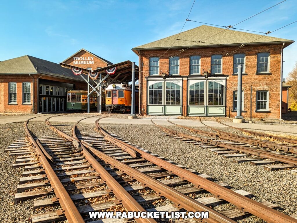 The Electric City Trolley Museum in Scranton, Pennsylvania, featuring the exterior of the brick museum buildings with large windows, multiple railway tracks in the foreground, and a clear blue sky above.