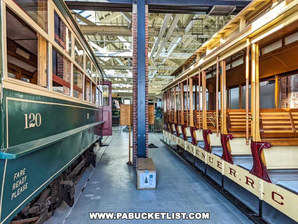 Side view of restored green and red trolley cars on display at the Electric City Trolley Museum in Scranton, Pennsylvania, inside a well-lit exhibit space with high ceilings and structural beams.