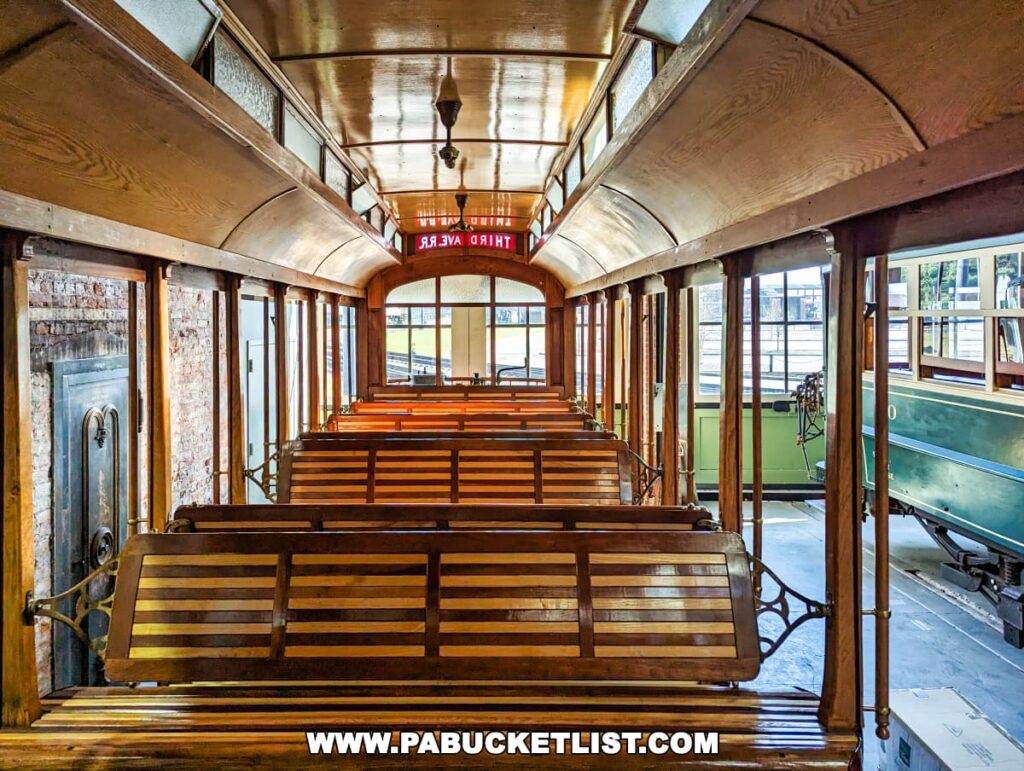 The interior of a vintage trolley with wooden seats and a curved ceiling, part of an exhibit at the Electric City Trolley Museum in Scranton, Pennsylvania, with the view extending out to the adjacent car and windows.