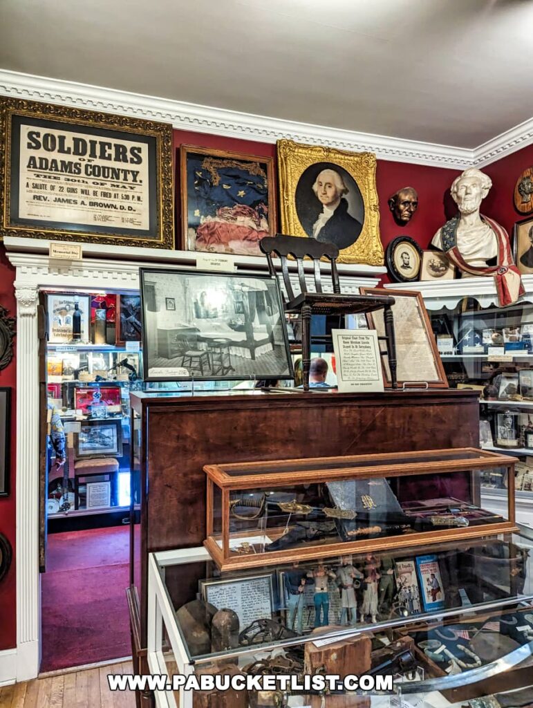 Interior view of the Gettysburg Museum of History displaying a rich collection of Civil War memorabilia. The walls are adorned with framed historical items including a 'Soldiers Adams County' poster, a damaged American flag in a golden frame, and a portrait of George Washington. A glass display cabinet contains various artifacts, and a wooden chair is visible in the foreground. Busts of historical figures and additional framed items enhance the exhibit.