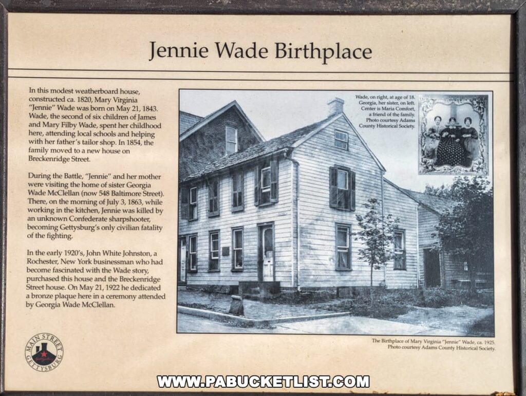 An informational plaque at Jennie Wade's birthplace in Gettysburg, Pennsylvania, providing historical details about her life and death. The sign includes an old photo of the weatherboard house where she was born and a family portrait. Text recounts her early years, her death during the battle, and the dedication of a plaque by John White Johnston in 1922.