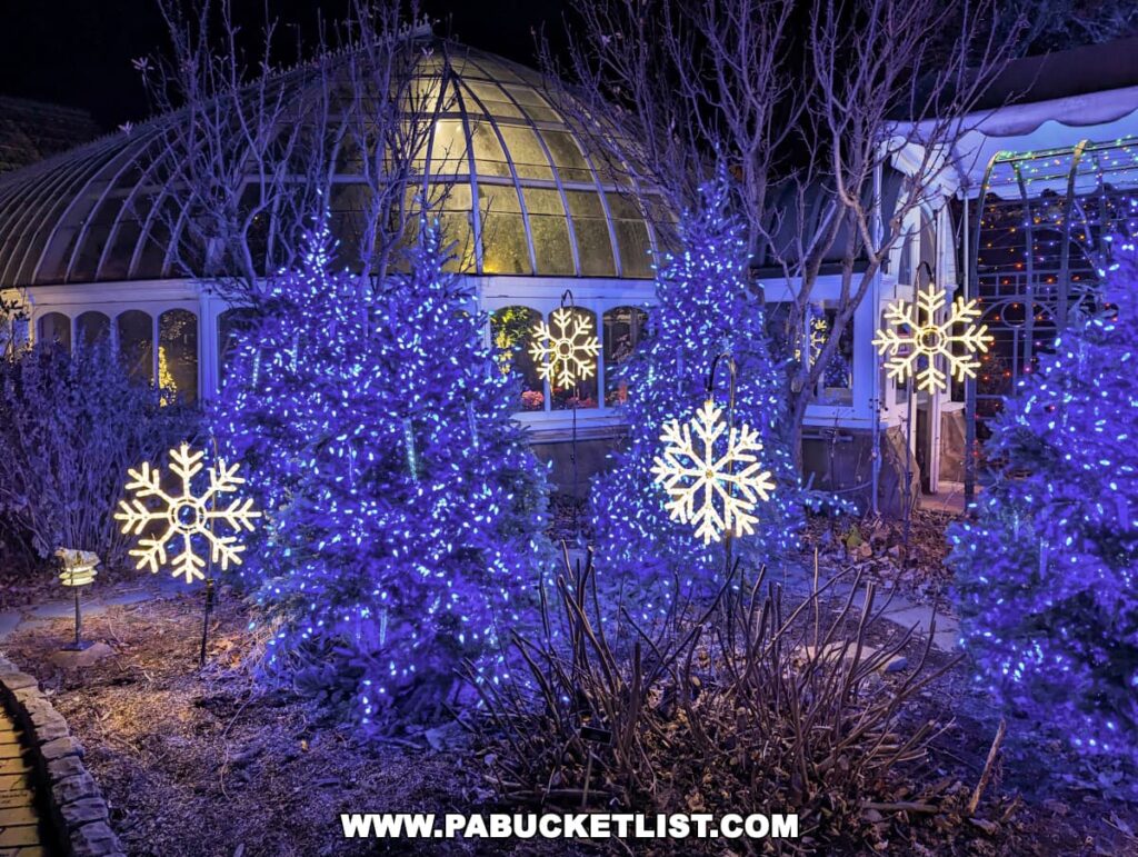 Vivid blue lights and illuminated snowflake decorations enhance the wintry theme outside the Phipps Conservatory during the Holiday Magic Winter Flower Show and Light Garden in Pittsburgh, with the glowing decorations contrasting beautifully against the conservatory's classic glass architecture in the evening.