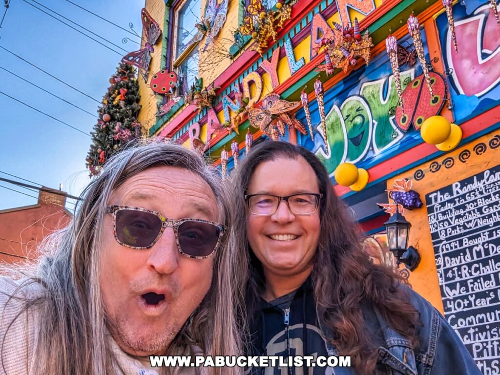 Randy Gilson, creator of Randyland, and Rusty Glessner, creator of PA Bucket List, with the vibrant and whimsical Randyland sign in the background.