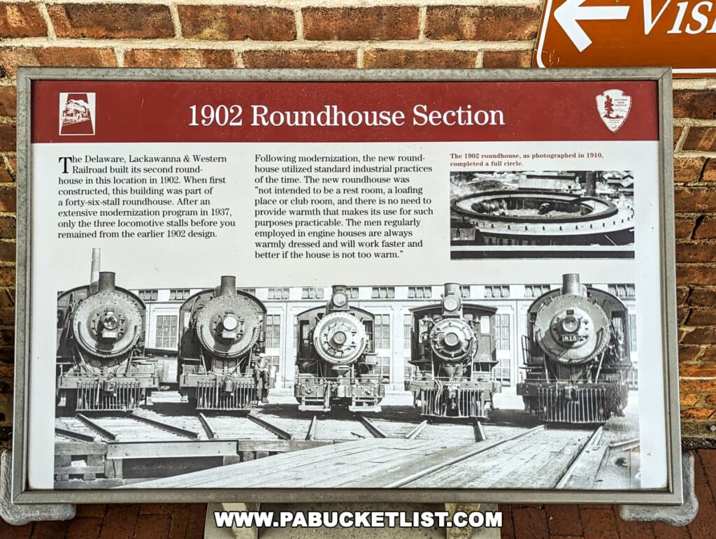 An educational plaque titled "1902 Roundhouse Section" at the Steamtown National Historic Site in Scranton, Pennsylvania. It includes a brief history of the Delaware, Lackawanna & Western Railroad's roundhouse and a black and white photo of three steam locomotives housed in the roundhouse stalls. An inset image shows the roundhouse as photographed in 1910. The text explains the building's purpose and the modernization that occurred in 1937. The plaque is mounted on a brick wall with a directional sign above pointing to the Visitor Center.