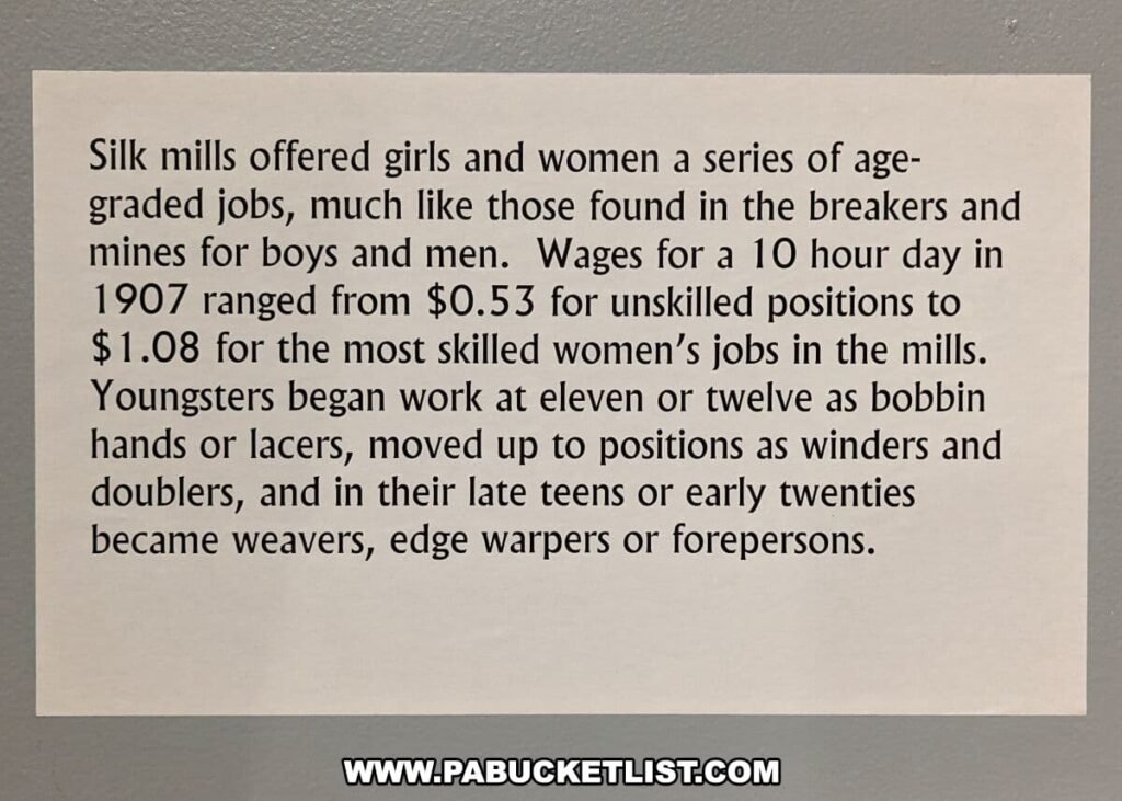 An informational text display at the Anthracite Heritage Museum in Scranton, PA, describing the work and wages of girls and women in silk mills in the early 1900s. The display outlines the range of wages from $0.53 for unskilled work to $1.08 for the most skilled women's jobs per 10-hour day in 1907. It also details the career progression for young workers starting from the age of eleven or twelve, from bobbin hands to weavers and forepersons, paralleling the employment structure of the coal mines for boys and men.