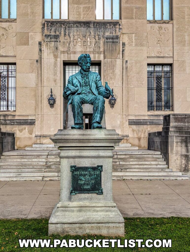 A bronze statue of Dr. Isaiah Fawkes Everhart seated on a chair, placed before the entrance of the Everhart Museum in Scranton, Pennsylvania. The museum's name is engraved above the entrance, with decorative engravings on either side of the name. The statue rests on a stone pedestal with a commemorative plaque.