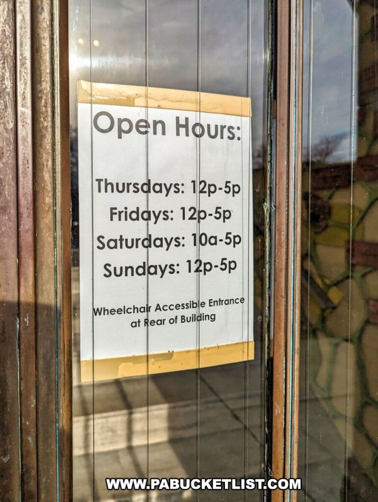 A sign displaying the open hours for the Everhart Museum in Scranton, Pennsylvania. The sign, placed on a glass door, reads "Open Hours: Thursdays: 12p-5p, Fridays: 12p-5p, Saturdays: 10a-5p, Sundays: 12p-5p". Below the hours, a note states "Wheelchair Accessible Entrance at Rear of Building" for accessibility information.