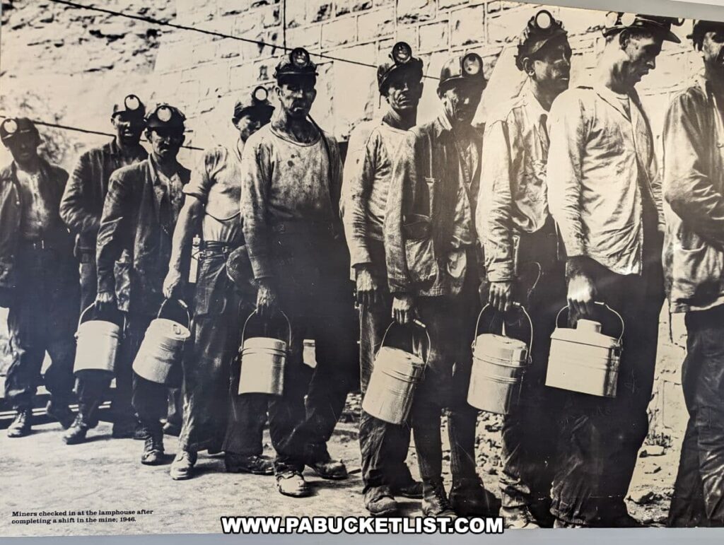 Historic black and white photo of a line of coal miners at the Lackawanna Coal Mine in Scranton, PA, circa 1946. Each miner wears a cap with a headlamp and carries a metal lunch pail. They stand in front of a brick wall, evidently at the end of a shift, as noted by the caption 'Miners checked in at the lamphouse after completing a shift in the mine, 1946.' Their clothes appear soiled from work, and they exhibit expressions of fatigue and resolve, reflecting the tough nature of their labor.