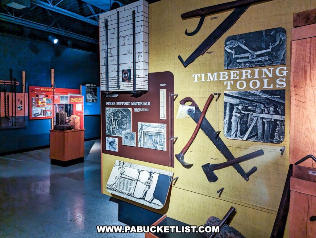 An exhibit on 'TIMBERING TOOLS' at the Museum of Anthracite Mining in Ashland, PA, displays an array of large, vintage tools used in mine timbering. Mounted on a mustard-yellow board, the tools include saws, axes, and drills, each essential for cutting and shaping the wooden supports that reinforced mine tunnels. Accompanying photographs and diagrams illustrate how these tools were used by miners. The exhibit is part of a larger display area with other mining-related exhibits in the background, creating an immersive environment for visitors to learn about mining operations.