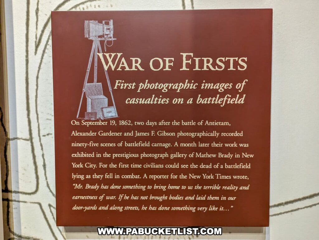The photo shows an informational display at the National Civil War Museum in Harrisburg, PA, detailing the "War of Firsts: First photographic images of casualties on a battlefield". It mentions that on September 19, 1862, two days after the Battle of Antietam, photographers Alexander Gardner and James F. Gibson recorded ninety-five scenes of the aftermath. A month later, these images were exhibited at Mathew Brady's gallery in New York City, marking the first time civilians saw photographs of battlefield casualties. The text includes a quote from a New York Times reporter about the profound impact of these images on the public's perception of the war. The panel serves as an educational piece on the role of photography in Civil War history.
