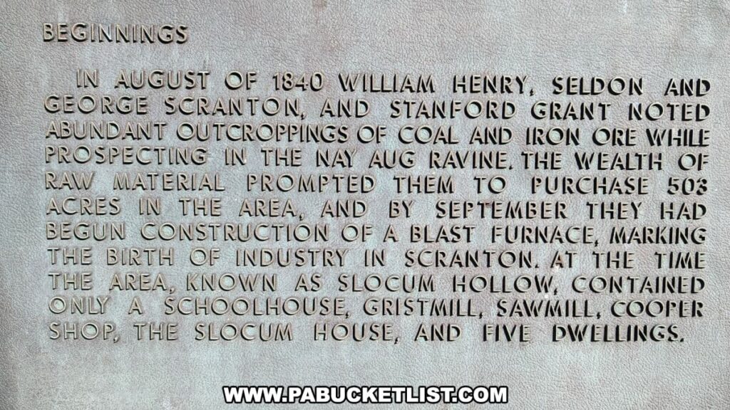A close-up of an informational plaque at the Scranton Iron Furnaces Historic Site in Scranton, PA, detailing the beginnings of industry in Scranton. The raised lettering on the plaque states that in August of 1840, William Henry, Seldon and George Scranton, and Stanford Grant discovered coal and iron ore while prospecting in the Nay Aug ravine, which led to the purchase of 503 acres and the construction of a blast furnace by September, signifying the birth of industry in the area known as Slocum Hollow, which at the time only had a schoolhouse, gristmill, sawmill, cooper shop, and five dwellings.