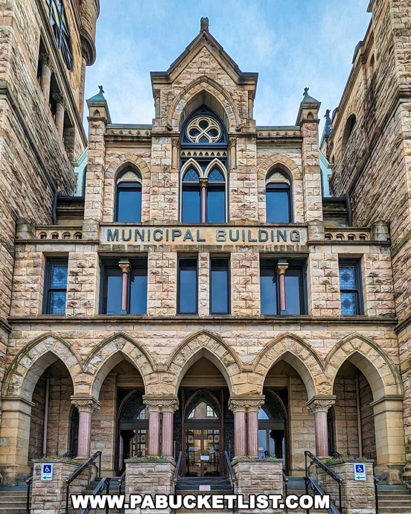 Front entrance of the Scranton Municipal Building in Pennsylvania, featuring Richardsonian Romanesque architecture with rough-cut stone, arched entrances, and pink granite columns. 'MUNICIPAL BUILDING' is engraved in stone above the central arch. The stately entrance and its historical design invoke the city's rich architectural heritage.