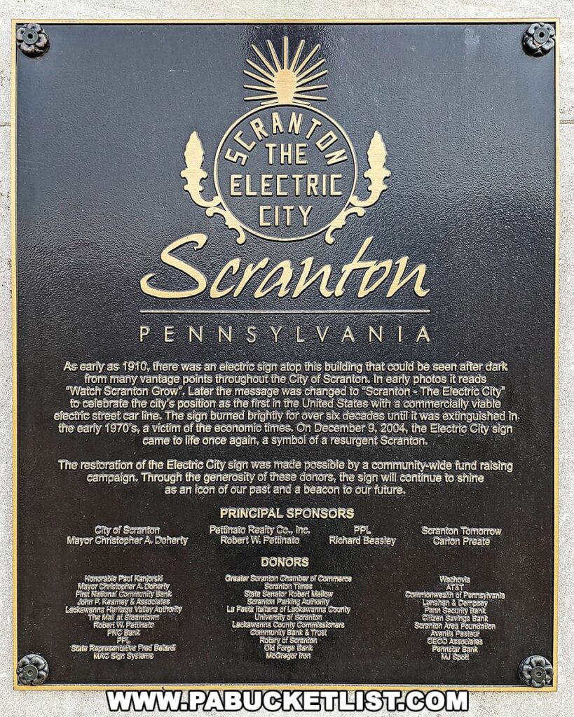 A plaque commemorating 'Scranton The Electric City' in Pennsylvania, detailing the history of the iconic electric sign first lit in 1910 and its significance to the city. The sign, which was restored in 2004, symbolizes Scranton's resurgent spirit. The plaque lists the principal sponsors and donors who contributed to the restoration, acknowledging their role in preserving this piece of Scranton's heritage.