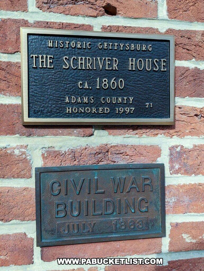 Two commemorative plaques mounted on a red brick wall at the Shriver House Museum in Gettysburg, Pennsylvania. The upper plaque, bordered in gold, reads "Historic Gettysburg The Shriver House ca. 1860 Adams County Honored 1997 71." The lower plaque states "Civil War Building July 1863," signifying the building's historical significance from the time of the American Civil War.