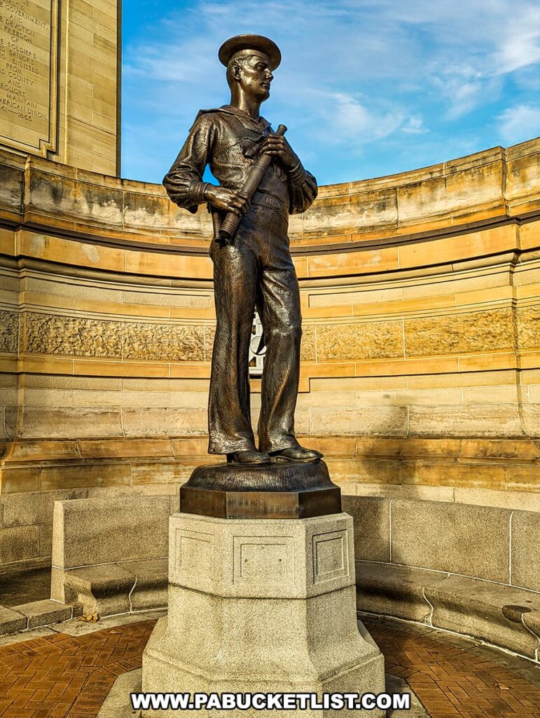 Bronze statue of a sailor called 'The Lookout' at the Soldiers and Sailors Memorial Hall and Museum in Pittsburgh, PA. The statue depicts a sailor in uniform, standing at ease with a pair of binoculars held near his chest. He is mounted on a stone pedestal and set against a curved stone wall, capturing the solemnity and vigilance of a lookout at sea.