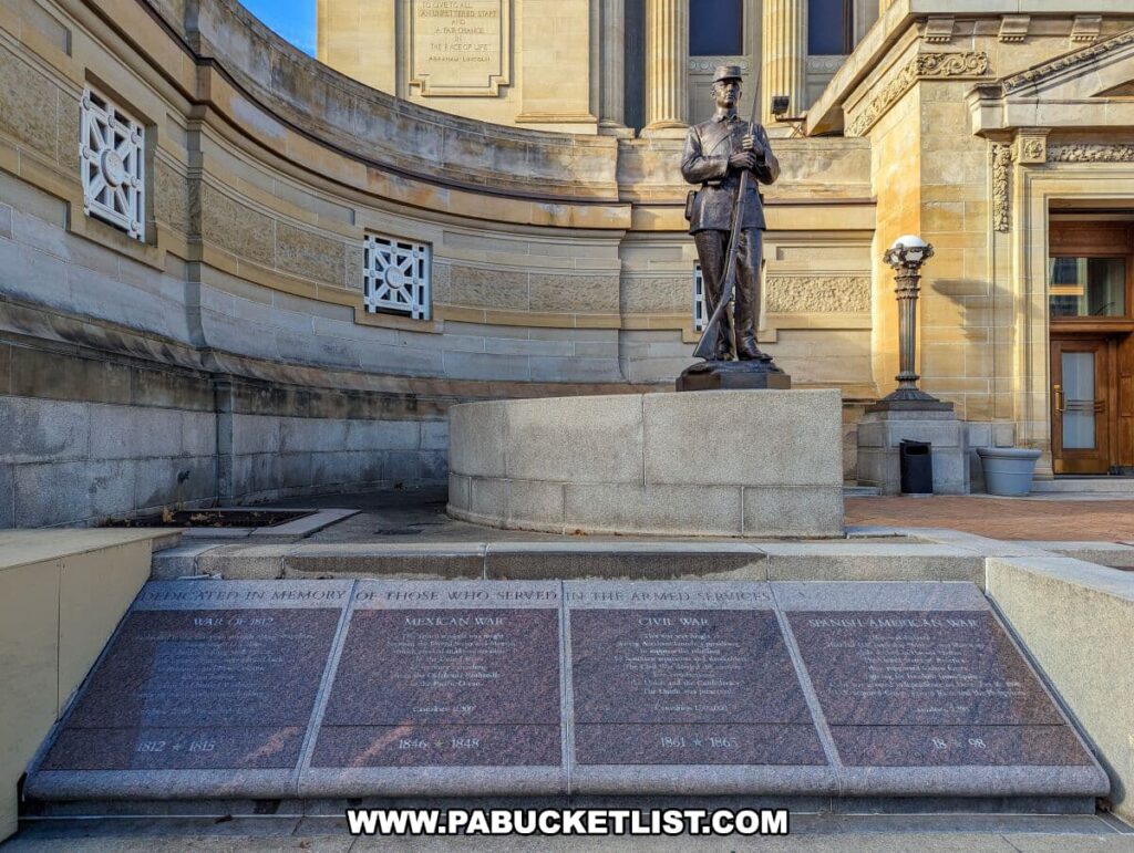 Bronze statue of a soldier titled 'Parade Rest' outside the Soldiers and Sailors Memorial Hall and Museum in Pittsburgh, PA. The figure is in full military dress, standing at the 'parade rest' position with a rifle. In the foreground, granite slabs list various American military conflicts, dedicated to those who served. The statue stands as a somber reminder of military service, positioned in front of the stately museum architecture.