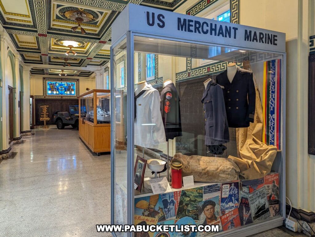 The US Merchant Marine exhibit at the Soldiers and Sailors Memorial Hall and Museum in Pittsburgh, PA, displaying naval uniforms, old maritime posters, and navigational tools. The exhibit, encased in a glass display, is situated in a hallway with intricate ceiling patterns, and a vintage military jeep can be seen in the background. The museum showcases the contributions of maritime service members through artifacts and historical narratives.
