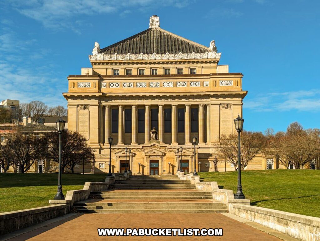 Frontal view of the Soldiers and Sailors Memorial Hall and Museum in Pittsburgh, PA, captured on a bright day. The grand building features a large set of steps leading up to its stately entrance, flanked by classical columns and sculptures. The intricate details of the façade and the expansive lawn in front highlight the architectural beauty and historical significance of this landmark.