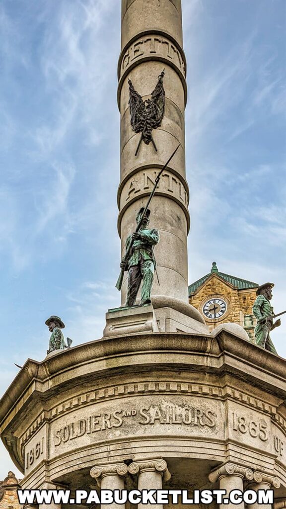 The Soldiers and Sailors Monument at Lackawanna County Courthouse Plaza in Scranton, Pennsylvania, features a tall column with inscriptions and bas-relief, topped with statues of military figures standing guard. The words 'SOLDIERS AND SAILORS 1861-1865' are etched into the stone. In the background, the clock tower of a historic building can be seen against the sky.