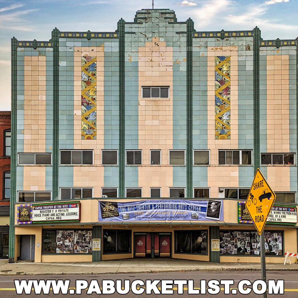 A photo of the Ritz Theater and Performing Arts Center in downtown Scranton, Pennsylvania. The facade of the theater is decorated in an Art Deco style, with a marquee at the top that advertises upcoming performances. In front of the theater, there is a sidewalk with a few people walking by.