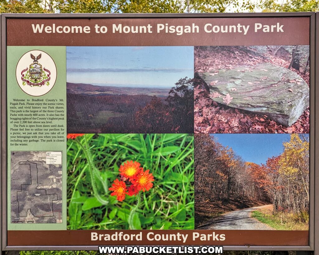 An informational sign at the entrance to Mount Pisgah County Park in Bradford County, Pennsylvania. The sign features a welcoming message, the park’s logo with the state's coat of arms, a map of the park, and several images depicting the natural beauty of the area. These images include a scenic vista, a rock covered in autumn leaves, a close-up of a vibrant orange flower, and a forested trail with fall foliage. Text on the sign provides a brief introduction to the park, its history, and an invitation to enjoy the facilities responsibly, noting the park's acreage and its status as the location of the county's highest peak. The bottom of the sign includes the text "Bradford County Parks".