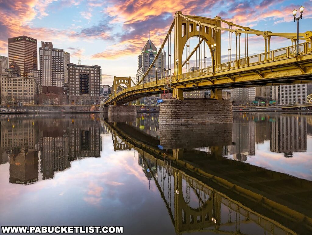 A sunrise view of the Pittsburgh skyline with the Roberto Clemente Bridge in the foreground. The bridge is reflected perfectly in the calm waters of the Allegheny River. The sky is a mix of warm and cool tones, indicating early morning light, and the city's buildings are illuminated by the rising sun. The scene captures the peacefulness of the city at dawn.