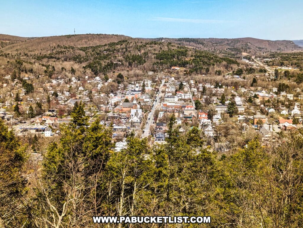 A scenic view of Milford nestled among rolling hills and dense forests. In the foreground, evergreen trees partially frame the panorama. The heart of the town is lined with neat rows of houses, their varying architecture hinting at a rich local history. Streets meander through the urban grid, converging towards a prominent church spire that punctuates the skyline. Beyond the town, a highway stretches into the distance, bisecting the hills and hinting at the gateway to further adventures. The landscape is a tapestry of natural and manmade harmony, typical of Pike County's picturesque terrain.