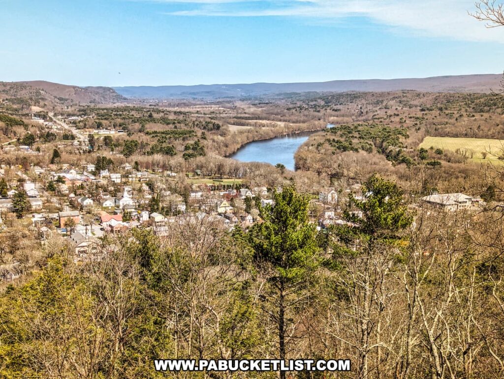 An expansive view from the Cliff Trail overlooking a valley in Pike County, Pennsylvania. In the center lies a serene blue river that meanders through the landscape, flanked by lush woodlands and a patchwork of fields. A small town sits closely huddled on one side of the river, its houses and buildings forming a cozy community tapestry amidst nature. The town stretches towards the forested hills that rise gently in the background, suggesting the peaceful coexistence of civilization and the wild. The scene is a showcase of the natural beauty characteristic of the Delaware River highlands.