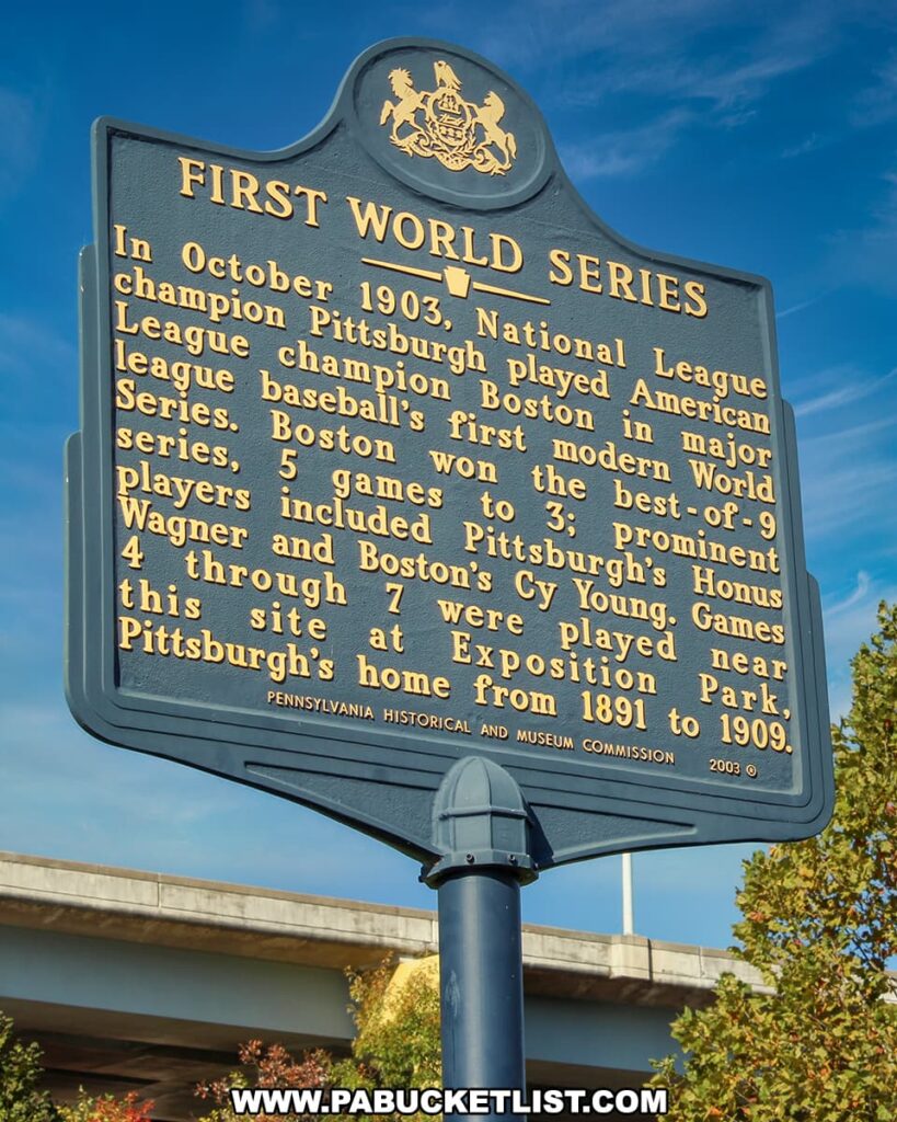 The image displays a Pennsylvania Historical and Museum Commission marker titled "FIRST WORLD SERIES," detailing the event of the first World Series played in October 1903. The text on the marker explains that the National League champion Pittsburgh Pirates played against the American League champion Boston in the first modern World Series, where Boston won 5 games to 3. It mentions prominent players such as Pittsburgh's Honus Wagner and Boston's Cy Young. The marker also notes that games 4 through 7 were played near this site at Exposition Park, Pittsburgh's home from 1891 to 1909. The historical marker is set against a clear blue sky, with a part of a bridge or overpass visible in the background, signifying its placement in an urban setting. This connects to the rich baseball history of Pittsburgh, leading up to the era of Forbes Field.